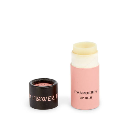 Pink tube with black cover. Cover has pink text saying, “Good Flower Farm”. Tube has black text saying, “Raspberry Lip Balm”.  Balm is an ivory color.