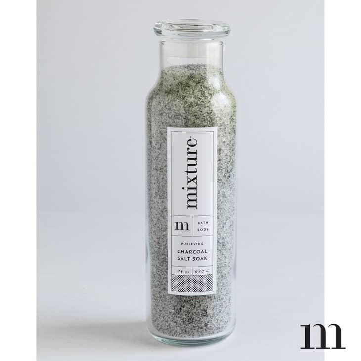 Charcoal scented ivory and black colored bath salt soak packaged in a tall glass bottle.