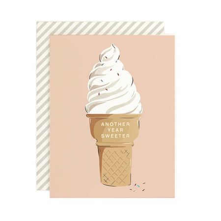 Pink card with white text saying, “Another Year Sweeter”. Image of a white vanilla soft serve ice cream cone with colored sprinkles. An ivory envelope is included.