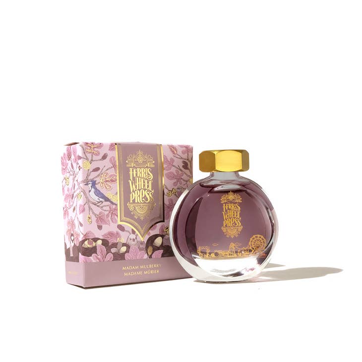 Round glass bottle with gold cover and gold text saying, "Ferris Wheel Press" with images of a carnival on front of bottle. Ink is purple. Packaged in square purple box with images of budding tree branches.