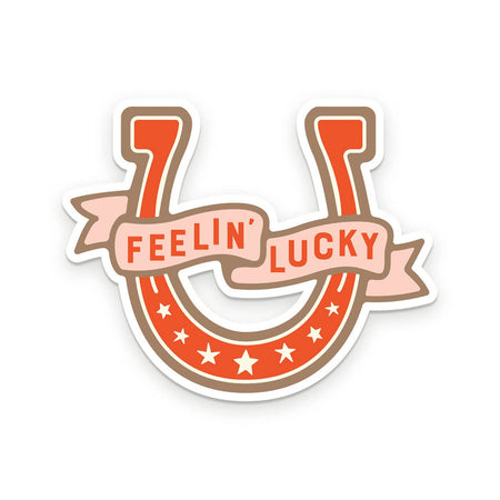 Sticker in the image of a brown horseshoe with a tan banner across the center saying, “Feelin’ Lucky” in brown text.