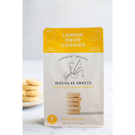 White package with yellow border on top with white and black text saying, “Douglas Sweets Vermont Bakery Scottish Shortbreads Lemon Drop Cookies”. Image of a stack of shortbread cookies and outline of a man playing bagpipes.