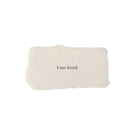 Gray rectangle with torn edges and black text saying, “I am Loved”.