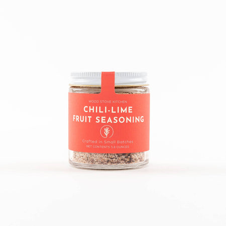 Small glass jar with tan colored seasoning with orange label and white text saying, “Chili Lime Fruit Seasoning”.