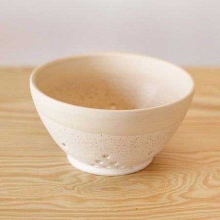 White and speckled tan ceramic bowl with decorative holes drilled into sides to function as a strainer for holding and washing berries.