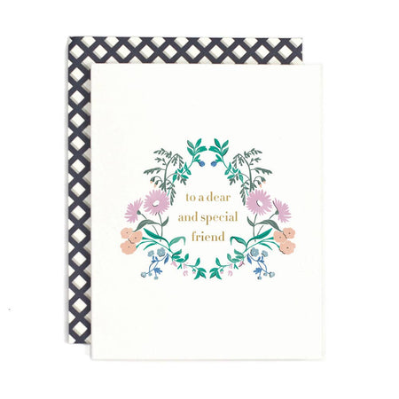 Ivory card with gold foil text saying, “To A Dear and Special Friend”. Image of a floral wreath with purple and orange flowers around text. An ivory and black tiled envelope is included.