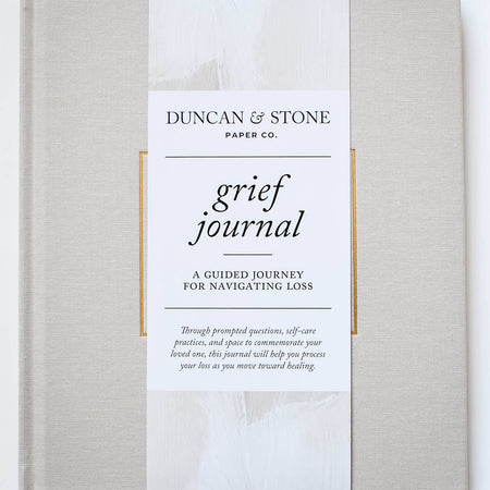Ivory color journal with gold foil text saying, “Grief Journal” in center.