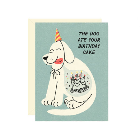 Blue card with black text saying, “The Dog Ate Your Birthday Cake”. Image of a white dog wearing a birthday hat and the image of a birthday cake inside its stomach. A cream envelope is included.