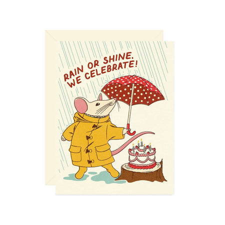 Ivory card with red text saying, “Rain or Shine, We Celebrate!” Image of white mouse wearing a yellow raincoat and yellow rain boots holding a red and white polka dot umbrella. A birthday cake sitting on a tree stump is next to mouse. A cream envelope is included.