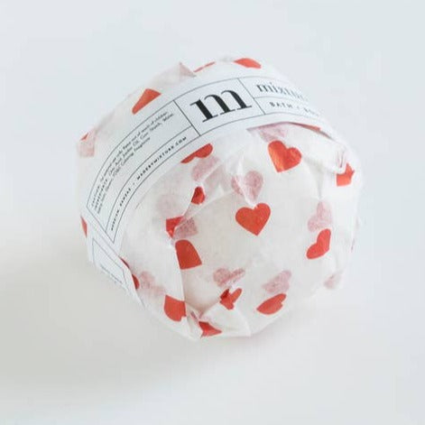 Circle ball wrapped in white packaging with red hearts and white label. Black text saying, “Mixture Bath & Body Valentine”.