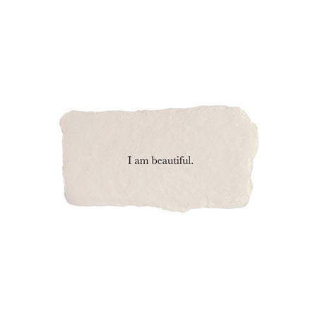 Ivory rectangle with torn edges and black text saying, “I am Beautiful”.