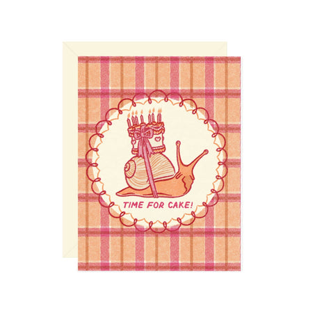 Card with a pink and orange gingham pattern background and image of a snail with a birthday cake strapped on its shell. Pink text saying, “Time for Cake!”. A cream envelope is included.