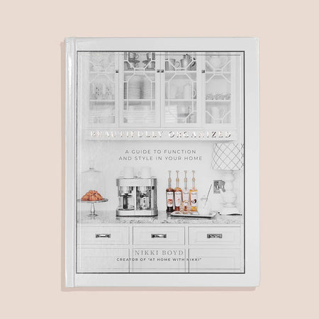 White cover with image of white kitchen cabinets and marble countertops with a coffee maker, wine bottles, lamp and cake stand with cookies. Black text saying, “Beautifully Organized A Guide to Function and Style in Your House”.