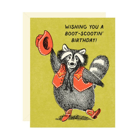 Green card with image of a raccoon dressed as a cowboy with red vest, red boots and a red hat. Black text saying, Wishing You A Boot-Scootin’ Birthday!” A white envelope is included.
