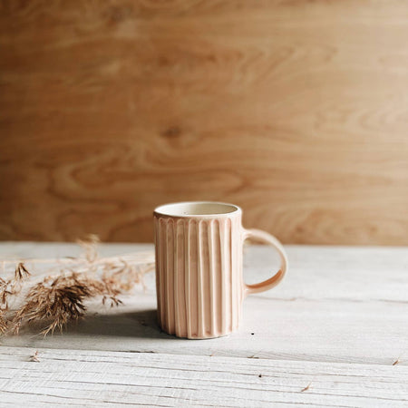 Peach color mug with vertical lines carved into mug with ivory handle on side.