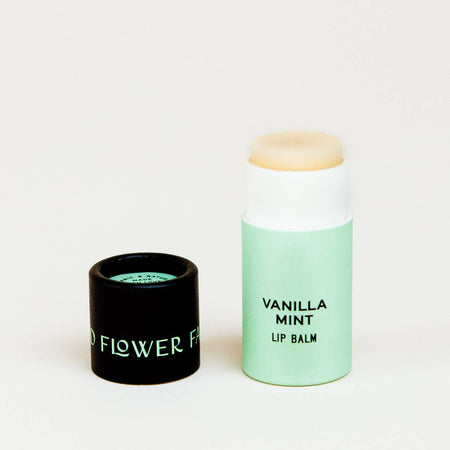 Mint green tube with black cover. Cover has mint green text saying, “Good Flower Farm”. Tube has black text saying, “Vanilla Mint Lip Balm”.  Balm is an ivory color.