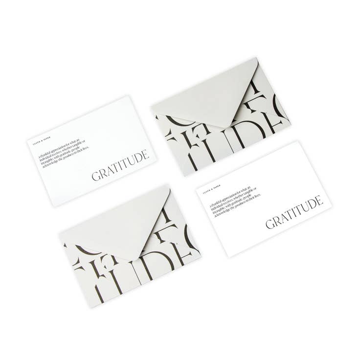 Notes of gratitude in black text on white cards presented in a gray envelope with black lettering spelling gratitude.
