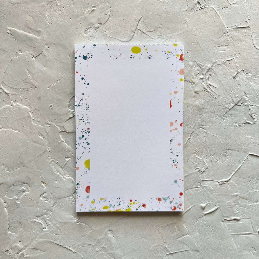 White vertical rectangle notepad with a border of colored paint splatters.
