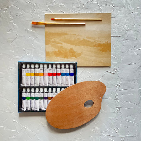 Painting kit with white canvas with tan landscape design; brown brush, brown palette and black case with various colored paint tubes.