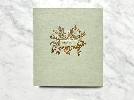 Binder with sage green cover with image of floral design and gold text saying, “Recipes”.