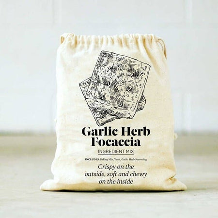Ivory drawstring bag with black text saying, “Garlic Herb Focaccia: Crispy on the outside, soft and chewy on the inside ”. Image of 2 slices of focaccia bread.