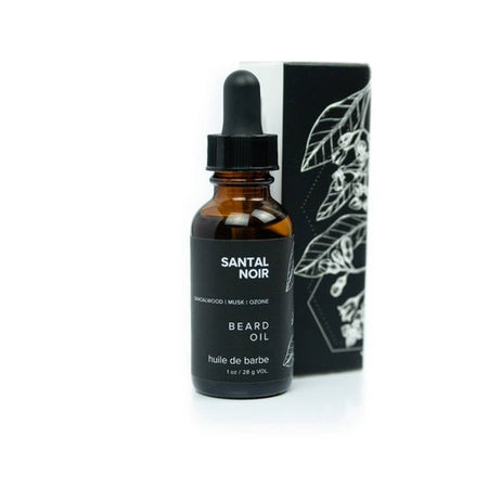Brown bottle with dropper top and black label with white text saying, “Santal Noir Charcoal Beard Oil”. Image of a white and black outlines leaves on side of label.