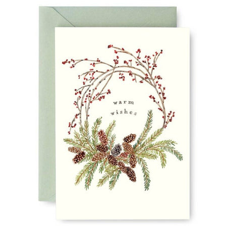 White card with image of a pinecone wreath with red berry branches on top. Black text in center saying, “Warm Wishes”. A green envelope is included.