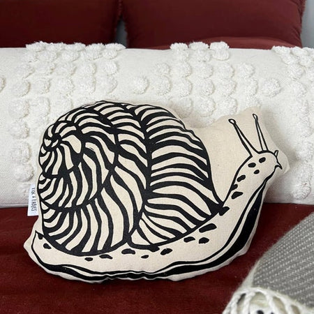 Decorative pillow with a snail design on a bed with red pillows and white blanket.