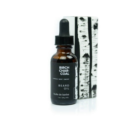 Brown bottle with dropper top and black label with white text saying, “Birch Charcoal Beard Oil”. Image of a white and black birch tree on side of label.