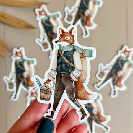 Sticker in the image of a fox wearing an outdoors outfit and carrying a bucket full of berries and branches.