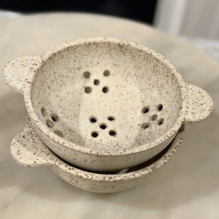 Small white speckled ceramic colander with holes.