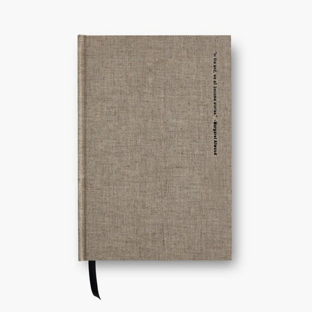 Journal with brown linen cover and black text saying, “In the end, we all become stories- Margaret Atwood”. Black ribbon bookmark in binding.