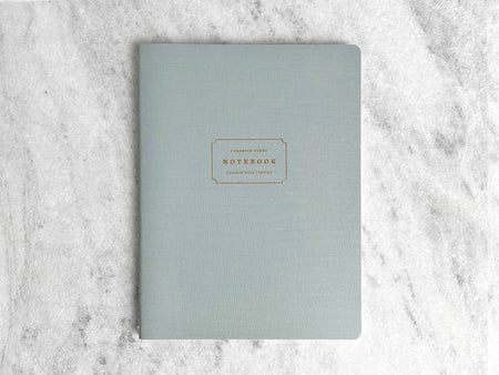 Notebook with light blue cover with gold text box in center with gold foil text saying, “Favorite Story Notebook”.