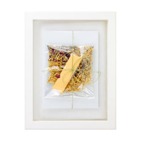 Paper kit including: white paper, yellow shreds of paper, yellow rectangle paper pieces, and dried flowers. Packages in a clear bag tied with a green ribbon.