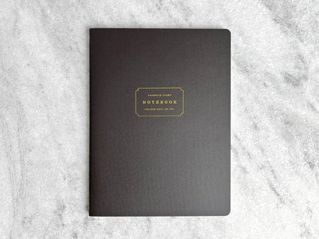 Notebook with black cover with gold text box in center with gold foil text saying, “Favorite Story Notebook”.