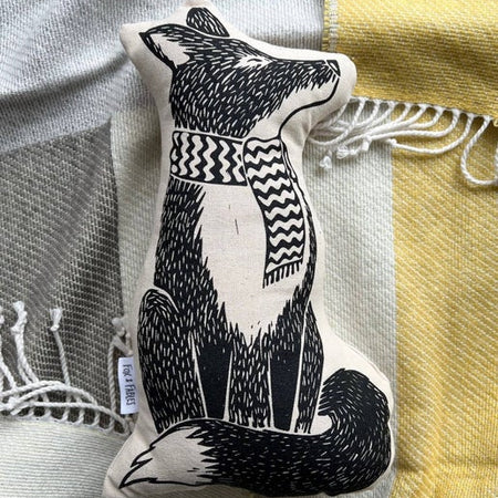 Black and white pillow in the image of a fox wearing a striped scarf.