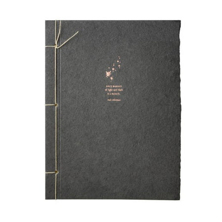 Charcoal black journal with torn edge cover and white ribbon binding on left side. Image of gold stars and gold text saying, “Every moment of light and dark is a miracle. Walk Whitman”.