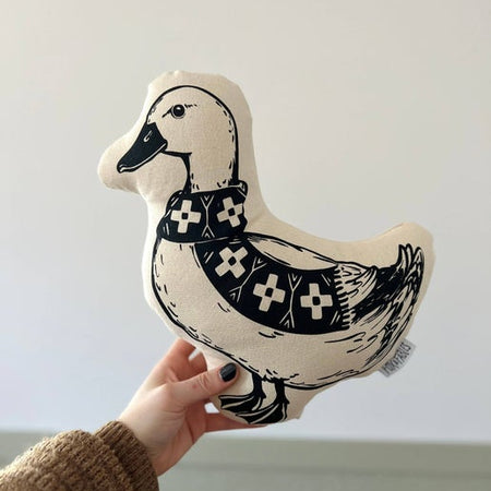 Black and white pillow in the image of a duck wearing a checkered scarf.