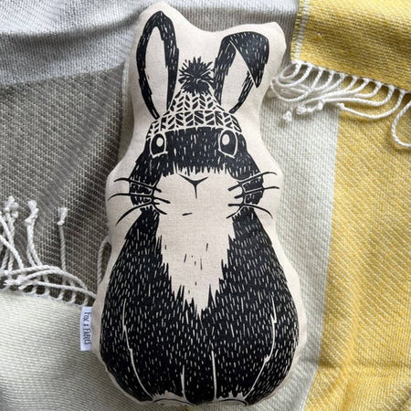Black and white pillow in the image of a rabbit wearing a winter pom pom hat.