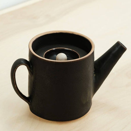 Small black ceramic teapot with lid, including a white ball in center of lid.