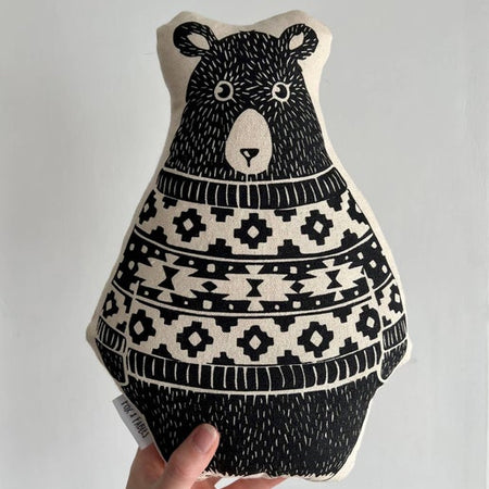 Black and white pillow in the image of a bear wearing a patterned sweater.