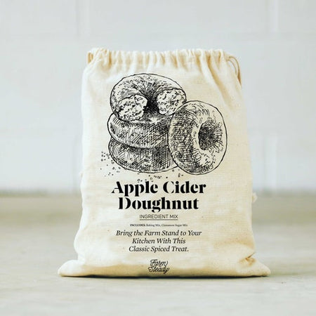 Ivory drawstring bag with black text saying, “Apple Cider Doughnut: Bring the Farm Stand to your kitchen with this classic spiced treat”. Image of 4 donuts, one with bit out of it.