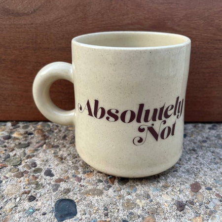 Ivory mug with tiny brown speckles and brown text saying, “Absolutely Not”.