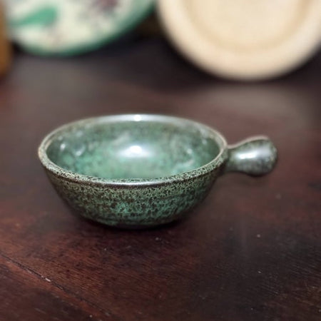 Small green bowl with wide handle speckled with brown flecks.