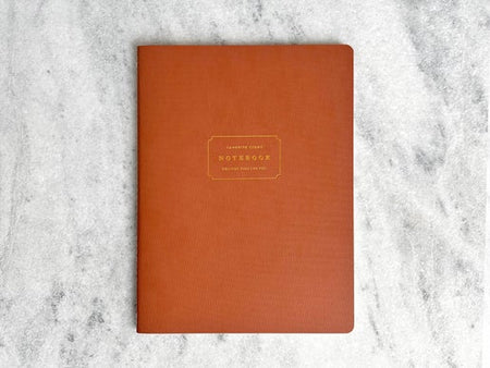 Notebook with burnt orange cover with gold text box in center with gold foil text saying, “Favorite Story Notebook”.