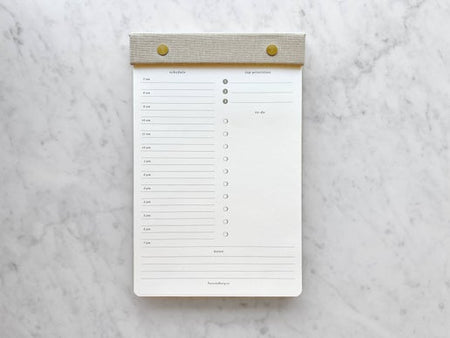 Off white daily calendar with gray leather binding across the top attached with brass screws.