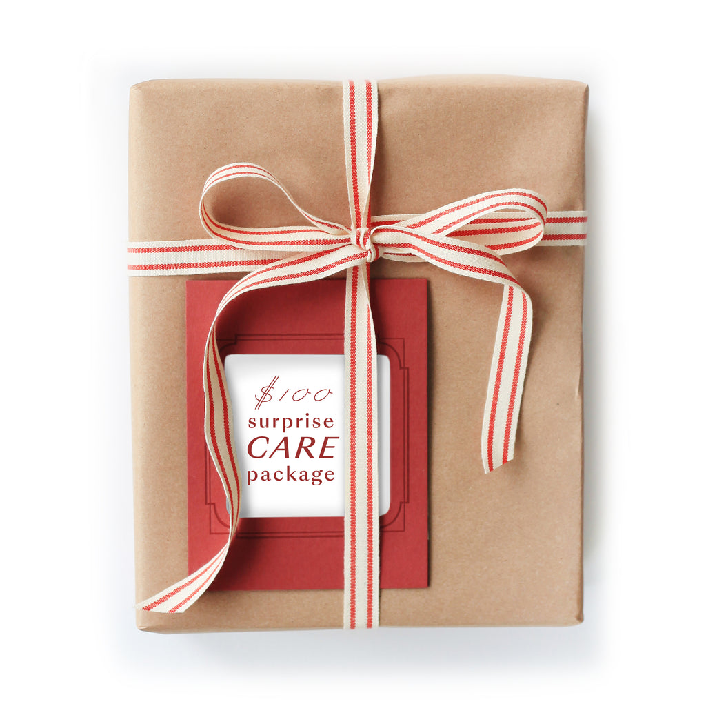 Rectangle package wrapped in brown kraft paper with a red and white striped ribbon and red card with red text saying, “$100 Surprise Care Package”.