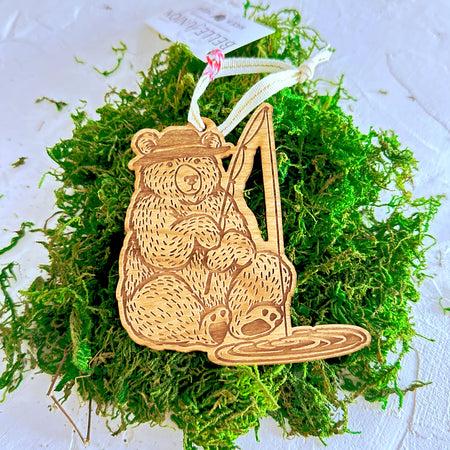 Wooden carved ornament of a bear wearing a fishing hat and holding a fishing pole.