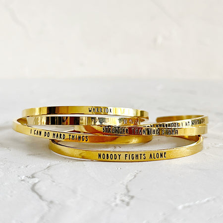 Gold band bracelet with black engraved text saying, “I Can Do Hard Things”.