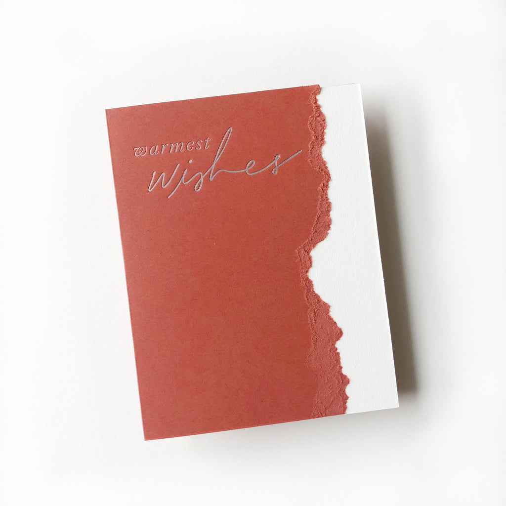 Red and white card with curved torn edging where the two colors meet. Silver foil text saying, “Warmest Wishes”. A white envelope is included.